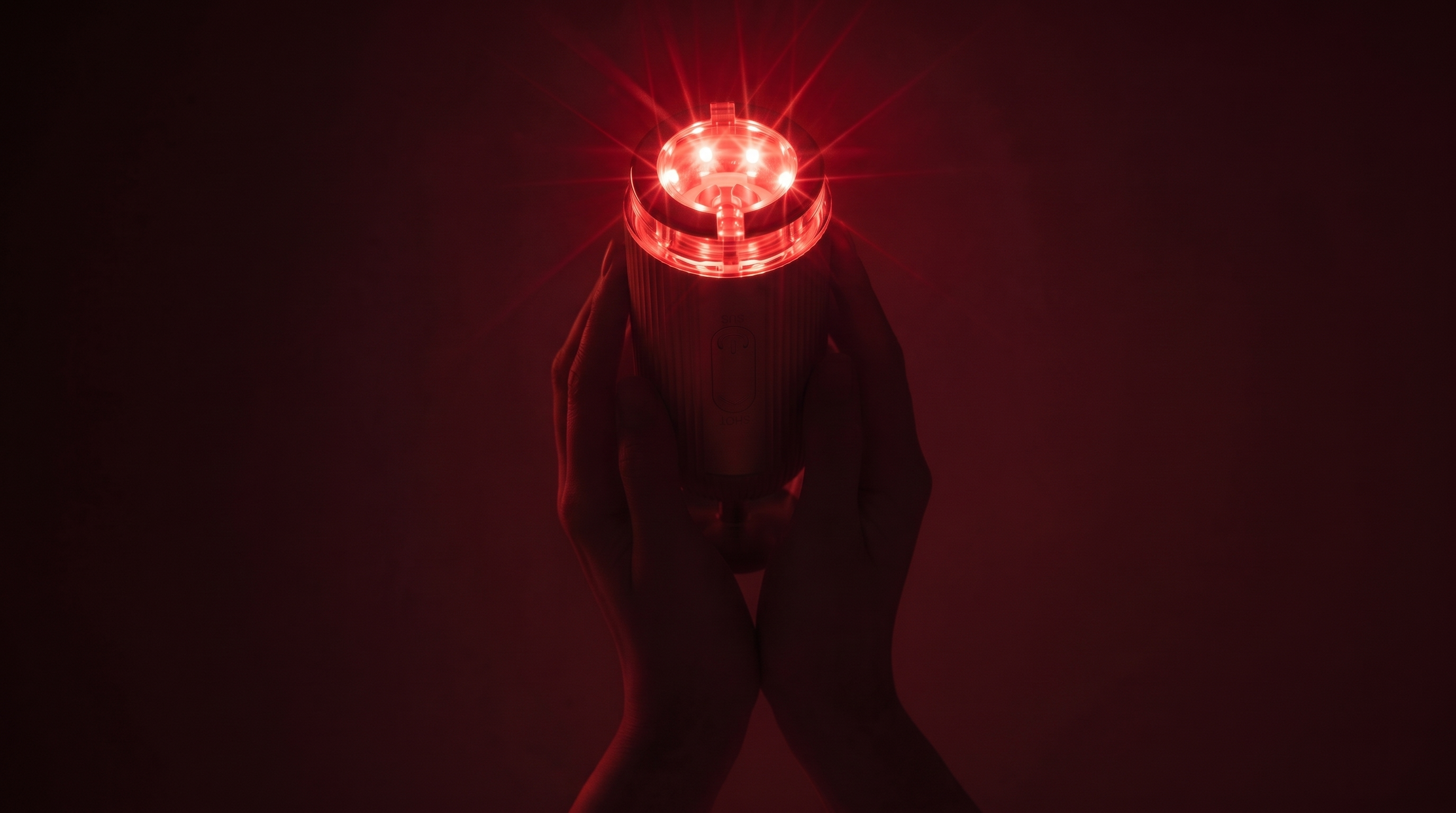 Gold FLOW+ device held in hands with red light against a dark background