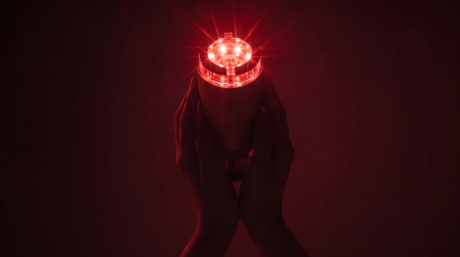 FLOW+ held in hands, with a softly glowing red treatment head